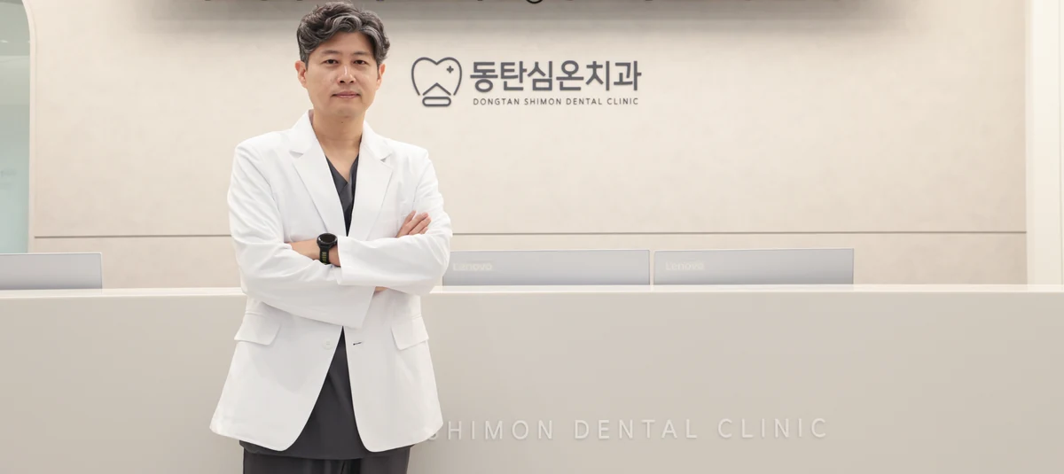 동탄심온치과 로고 벽 앞에 선 치주과 전문의 심재용 대표원장